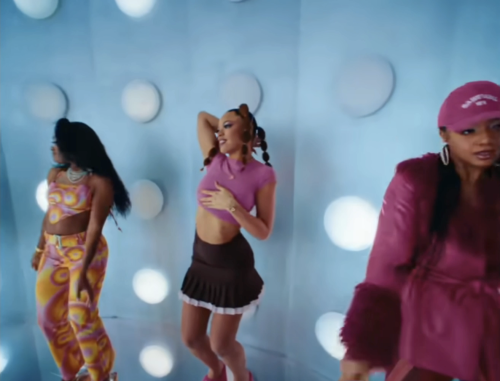 Three of the women, swirl two-piece, pink crop top, and pink leather jacket dance in front of the wall.