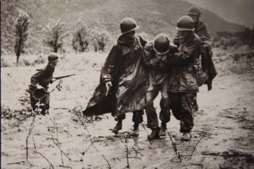 Chaplain (Capt.) Emil Kapaun (right) and a doctor carry an exhausted Soldier off the battlefield in 