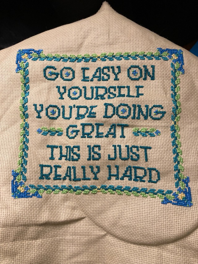 finished cross stitch on beige aida, with green and blue thread; reads "go easy on yourself you're doing great this is just really hard"