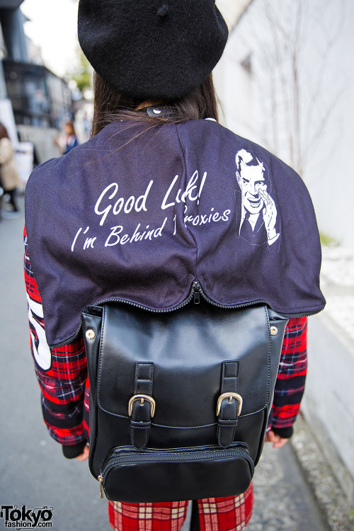 17-year-old Aria on the street in Harajuku wearing a plaid outfit with a jacket that says “Goo