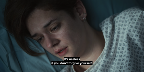 Text reads: It's useless if you don't forgive yourself. An aerial close-up of a white woman with short brown hair laying in bed wearing small silver earrings and a hospital gown. She looks like she has been crying.