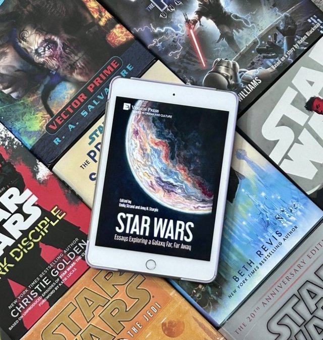 Pictured is an ereader with the ebook of Star Wars: Essays Exploring a Galaxy Far Far Away (Vernon Press, 2023, edited by Emily Strand and Amy H. Sturgis) on top of other Star Wars books. The image is from Now This Is Lit: A Star Wars Books Podcast.