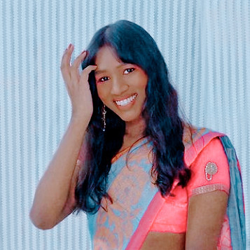 kali, a dark skinned trans woman from hyderabad, india, smiles at the camera while adjusting her hair. she wears a pale blue saree with a bright pink blouse, and long earrings. 