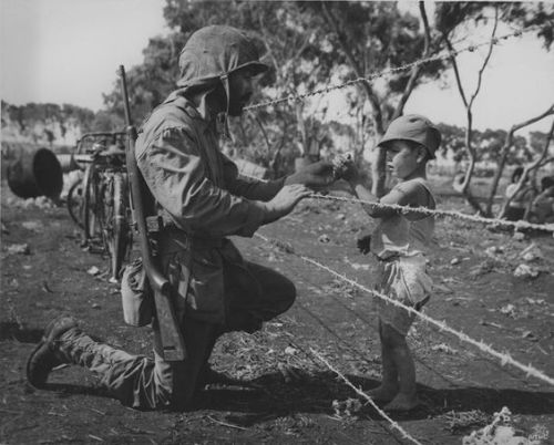 A US Marine giving candy to a child interned by the Japanese on Tinian, 1944, World War II.