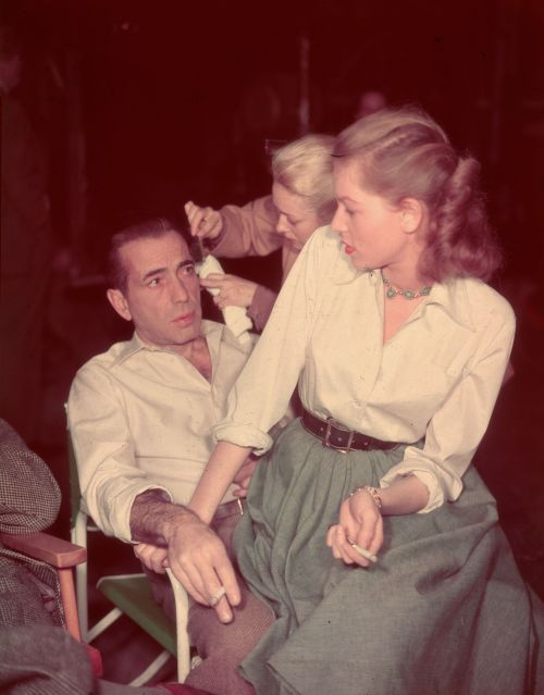 vintageeveryday:Lauren Bacall sits in the lap of Humphrey Bogart, both holding cigarettes, on the se