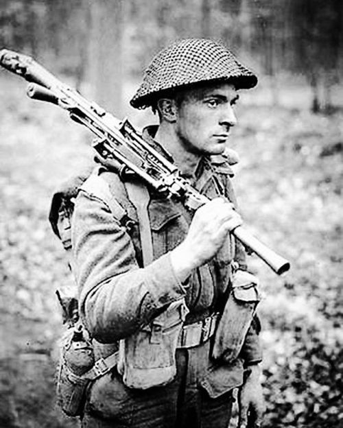 Pvt H.E. Goddard of the Perth Regiment carrying a Bren LMG as he advances through a forest north of 