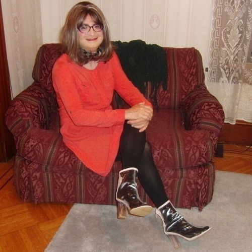 Full-length picture of me, seated, legs crossed, knees left, wearing my new purple cat-eye glasses, 