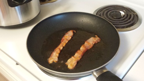 a frying pan with two slices of frying bacon.