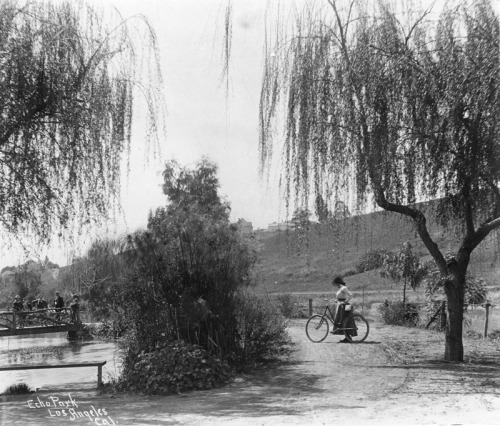 A woman pushing her bicycle through rustic Echo Park, Los Angeles,1900.