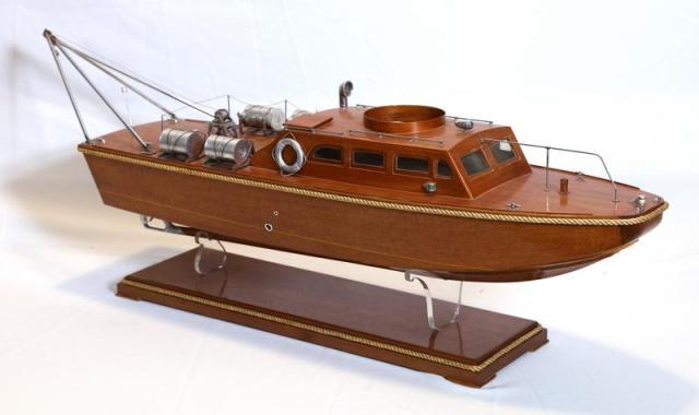 A scale model of a fully equipped Patrol Torpedo (PT) boat. The boat is made of lightly stained wood and metal fixtures. The model sits on a pair of clear plastic cradle stands attached to a stained wood base with rope trim.