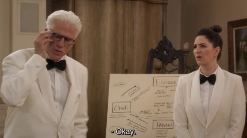 Michael and Janet in caterer’s uniforms. Michael says “Okay.”