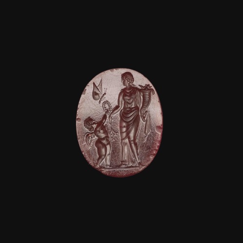 ancientjewels:Roman carnelian intaglio gem depicting the goddess Fortuna with a cornucopia, Eros wit