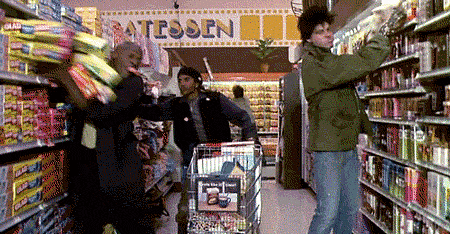 Three men throw many items into a supermarket shopping cart.