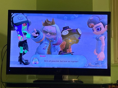 three octolings and an inkling stand together as the inkling strikes a happy pose, one looks emotionless (the player), the other is happy and looking at the inkling (Marina), the green-skinned one (Acht) is just proud of the inkling (Pearl), as the chat bubble reads for Pearl "We're gonna kick that loser out together!"