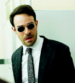 A clearly frustrated Matt Murdock licking his lips then pointing his fingers towards someone