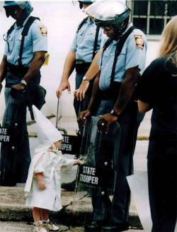 sogaysoalive:  This powerful image came up over 20 years ago and taken by Todd Robertson during a KKK rally in northeast Georgia, USA. One of the boys approached a black state trooper, who was holding his riot shield on the ground. Seeing his reflection,