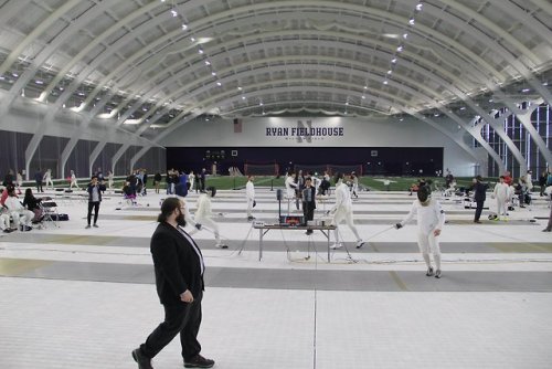 [ID: two photos of a fencing tournament, held in a second-story fieldhouse. Half of the indoor field