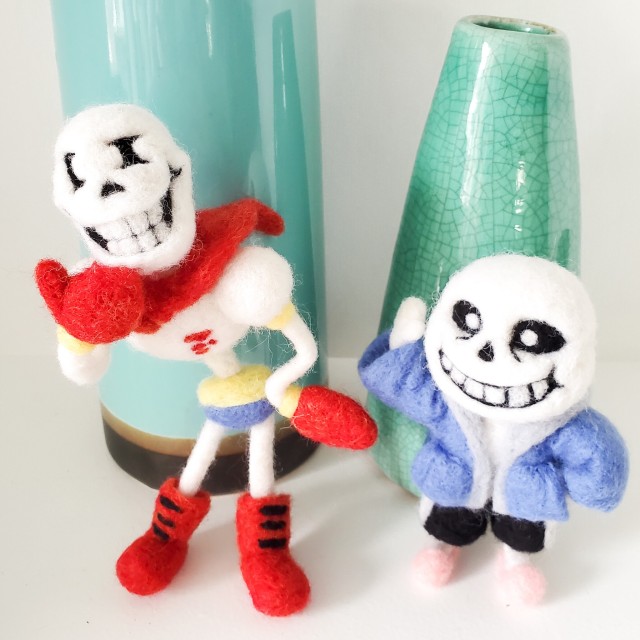 A photo of needle felted Papyrus and Sans. Papyrus has his left wrist on his hip and his right hand on his chin. Sans has his left hand in his pocket and one hand held up next to his head.