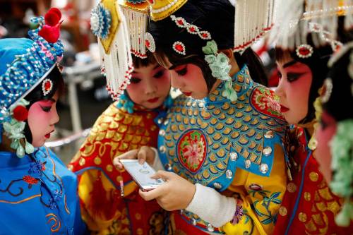 fotojournalismus:A participant plays a game on her phone as others watch during a break in a traditi