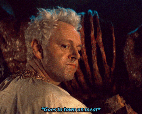Gif of a scene from the Good Omens season 2 episode 2 minisode where Aziraphale is eating ox in the basement of Job's house. He looks at Crowley before he ravenously continues eating. The subtitles say: *Goes to town on meat*