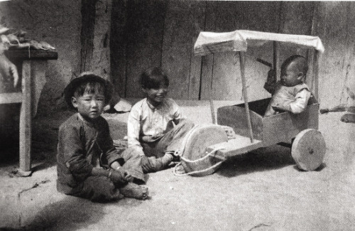 Siblings playing in front of their family shop in Qinghai in 1941. The youngest is sitting in a thre