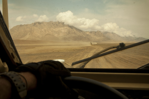 Majestic mountains, dangerous desert. Coalition force tactical vehicles move across the desert depar