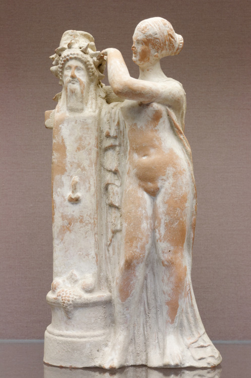 lionofchaeronea:Terracotta statuette, depicting Aphrodite crowning a herm of Dionysus.  Artist unkno