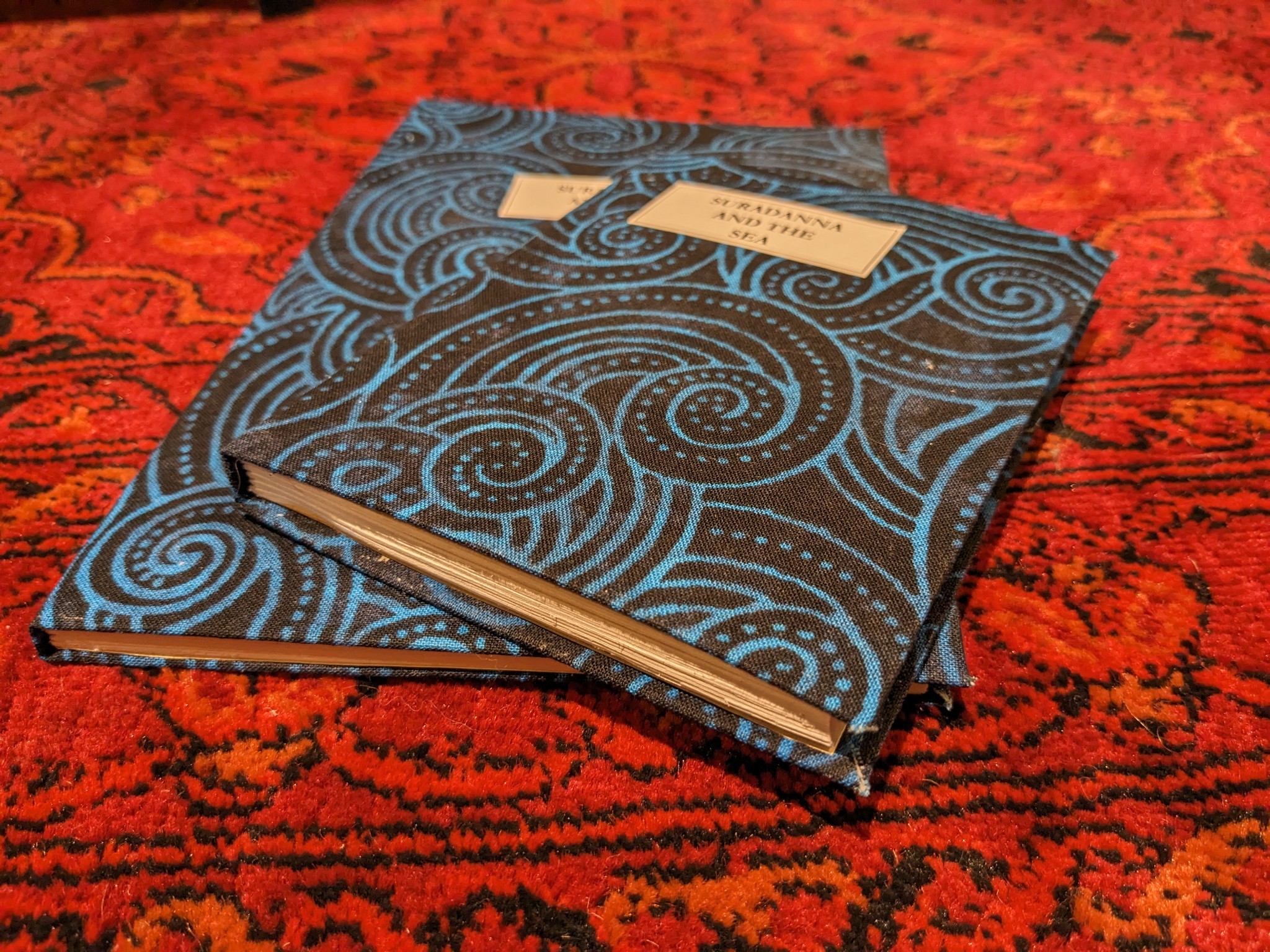 photo of two hand-bound books with blue and black swirled covers entitled SURADANNA AND THE SEA