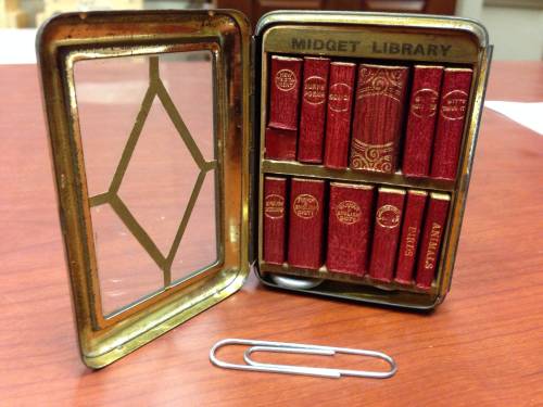 12 volumes in metal case with glass front, resembling miniature bookcase; miniature magnifying glass