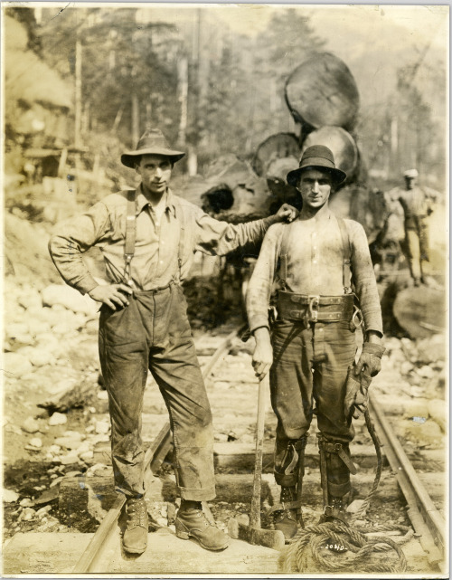 askhistorians:A high rigger holding an axe standing beside another employee of the Capilano Timber C