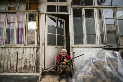 An armed woman sits at the entrance of her home during the shelling near the city of Stepanakert in 