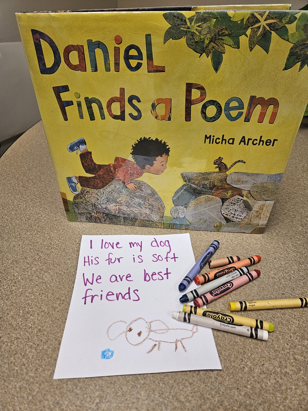 The book cover shows a child laying on a rock face to face with a chipmunk. In front of the book is a scattering of crayons and a paper that reads I love my dog. His fur is soft. We are best friends. with a drawing of a dog