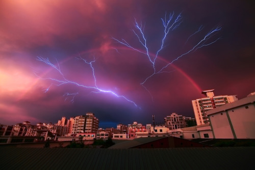 sixpenceee:    A rainbow appears in the sky as lightning strikes during a rainstorm on May 13, 2012 in Haikou, China. Photo credit: China Foto 