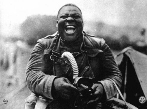 An African American soldier of the 366th infantry laughing while holding a gas mask, World War I.