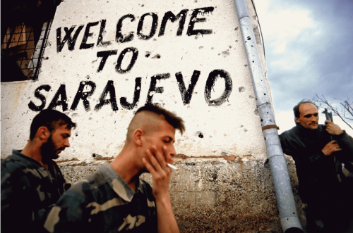 Bosnian soldiers smoke and take a break on the front line next to a sign that says, “Welcome to Sara