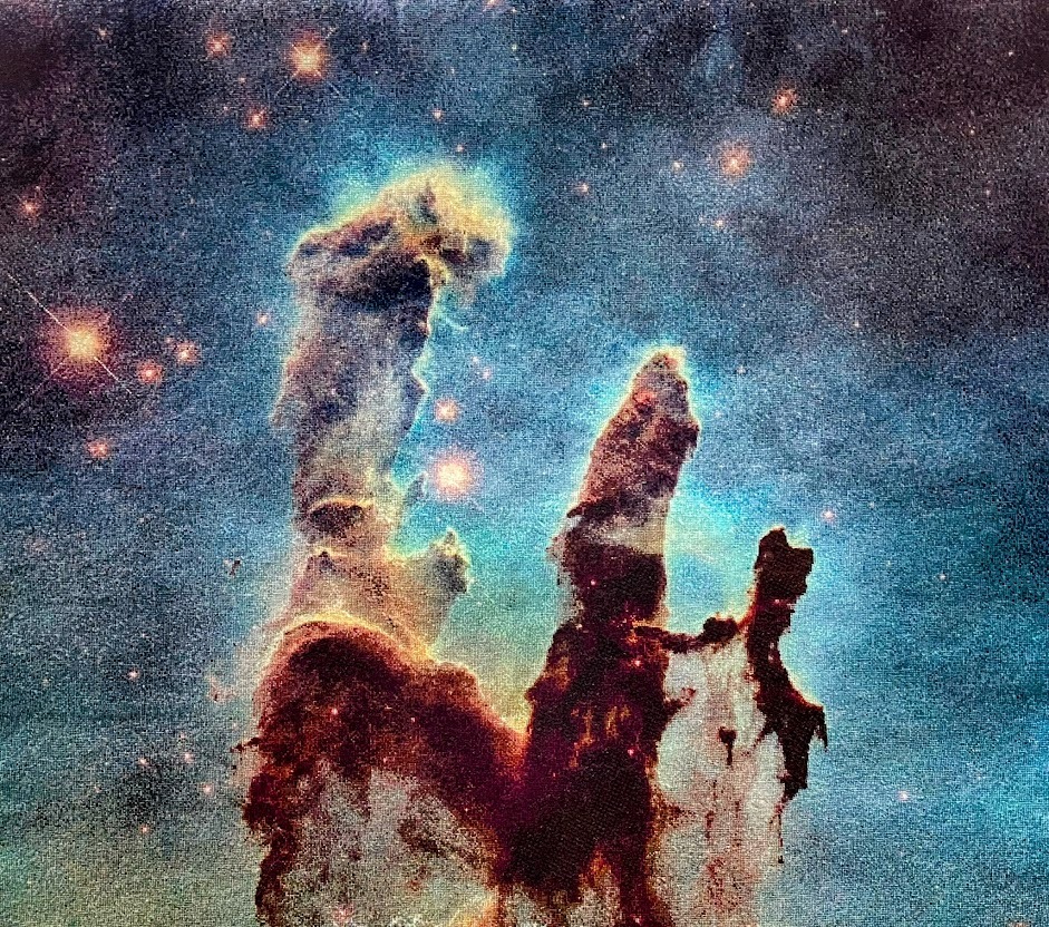 This embroidery piece shows the Pillars of Creation inspired by the Hubble Telescope. The design is on a vintage embroidery frame (circa 1905)  with brown yarn on each side. In the middle a white tapestry shows the galaxy. There are three towering tendrils of cosmic dust and gas sitting at the center of the piece, colored in red and white. On the outside, space is blue with stars bursting in red colors.  Credit: Melissa Cole, Star Stuff Stitching