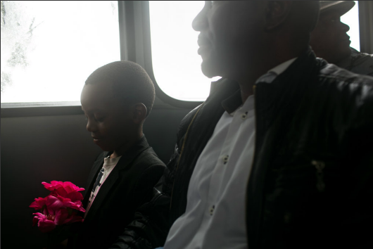 Shoun Ngene, 6, held plastic flowers he brought for the Mandela memorial while riding a shuttle bus to the stadium with his father, Emmanuel (Photo by Todd Heisler/NYT)