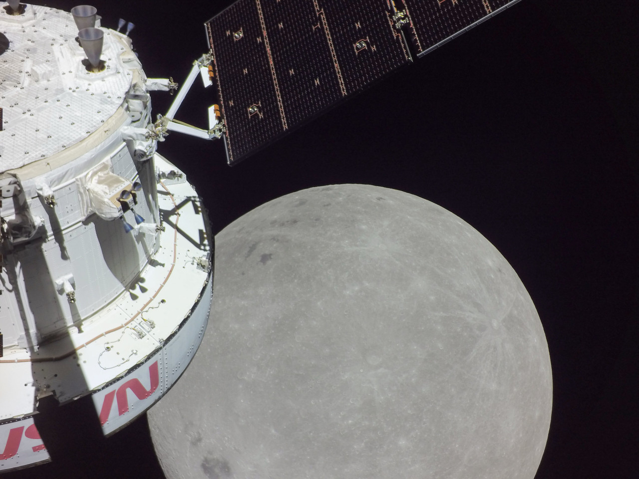 A portion of the far side of the Moon looms large just beyond the Orion spacecraft in this image taken by a camera on the tip of one of Orion’s solar arrays. The Moon can be seen against the darkness of space on the right side of the image. On the left side of the image, part of the Orion spacecraft can be seen, with its dark-colored solar array jutting out from the European Service Module. Credit: NASA