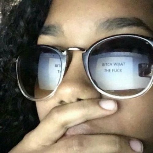 Some person wearing sunglasses that show a reflection of a computer with "Bitch what the fuck" written on a blank white backround. The person has their hand over their mouth like they're shocked.