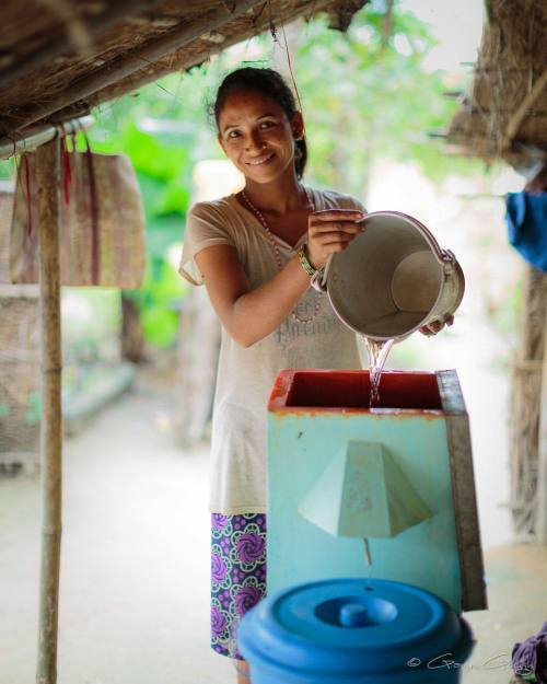 Bisnu replenishes the biosand water filter outside her family...