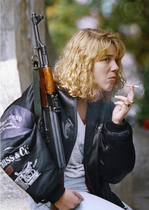 A Bosnian girl, holding an AK-47 rifle smokes a cigarette as she waits for a funeral service at Sara