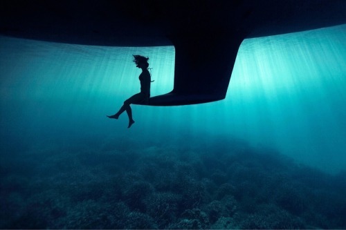 sixpenceee:  A photograph of a girl sitting on the keel of a boat underwater