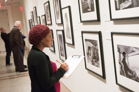 Student taking notes on photography display in a gallery setting