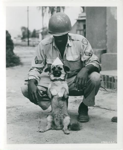 Sergeant Flanagan, the adopted mascot of the Fifth Air Force Base, models a paper hat which Sergeant Milton Turner (Brownsville, OR) made/1 Aug 1950