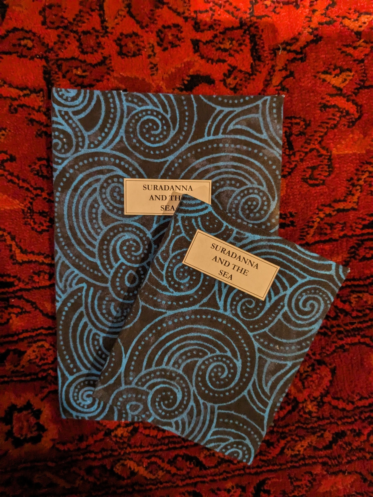 photo of two hand-bound books with blue and black swirled covers entitled SURADANNA AND THE SEA