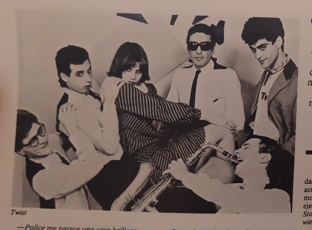 A black and white photograph from a magazine of the 80s of a group of six people who are probably in a music band and are posing in the same way as the characters above.