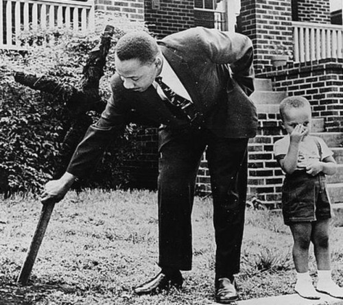 Dr. Martin Luther King Jr. takes down a burnt cross from his lawn as his son stands next to him, 196