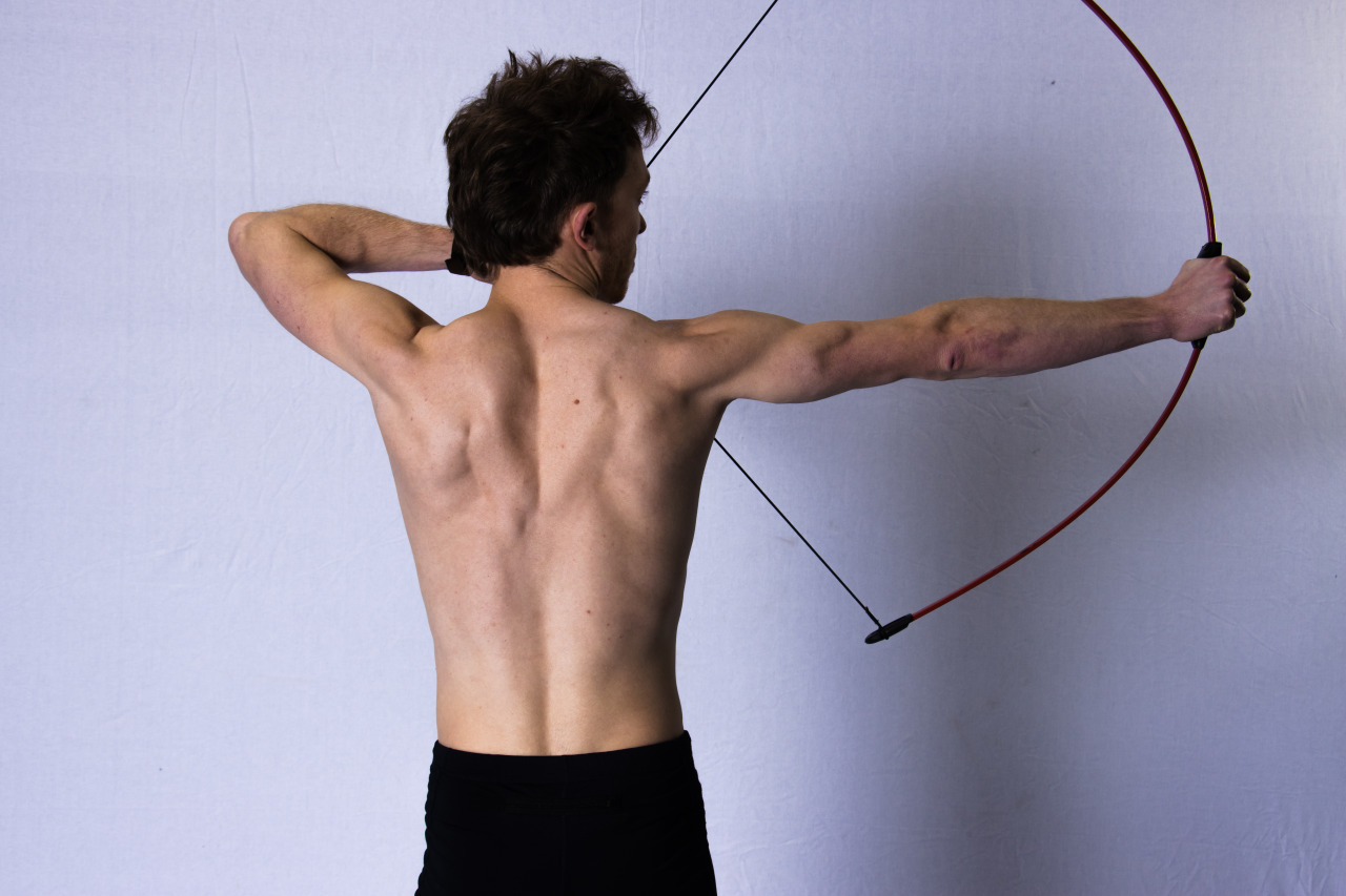 A photograph of a shirtless man drawing a 12lb bow, showing muscle engagement.