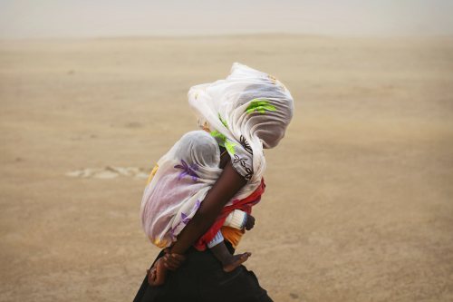 A woman carrying her baby and wrapped with a shawl walks through a sandstorm in Timbuktu on July 29,