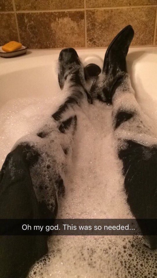 A picture of a person’s legs in a bath with soapy water. The person is wearing black slacks and dress shoes, implying they’re wearing a suit. Text reads “Oh my god. This was so needed…” End Image ID.